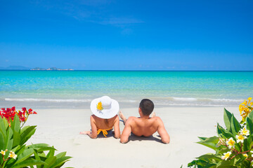 Fototapeta na wymiar Young couple resting on a tropical beach on a summer sunny day on a background of clear blue sky and turquoise sea.
