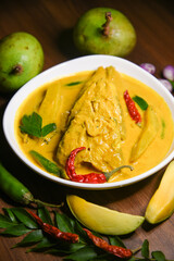 Kerala fish curry, spicy and hot king fish mango curry with green curry leaf Kerala India. Top view Barracuda Fish curry with green chili, coconut milk and mango Asian cuisine.

