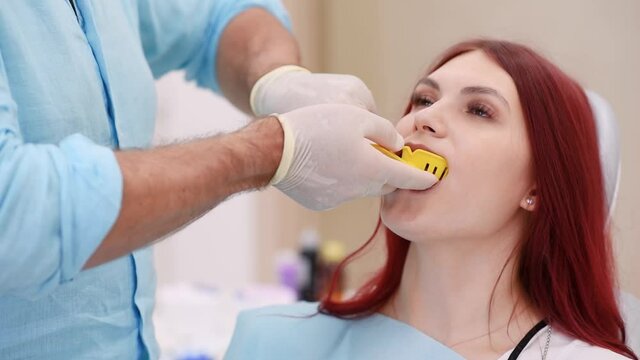 The orthodontist shows the patient an impression tray in which the silicone impression material will be placed to get the shape of her teeth