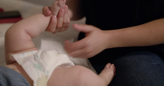 Close view of physiotherapist stretches little newborn baby's legs on bed