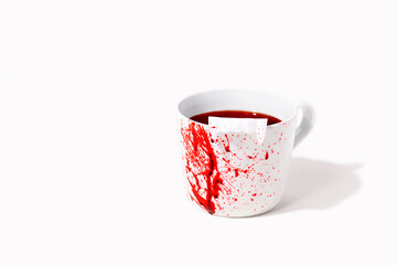White cup with fake blood splatter and toy dracula teeth on white background with copy space. Creative concept for Halloween