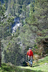 Fototapeta premium fly fisherman trout fishing with a hiking backpack and an orange jacket in the high mountains in summer