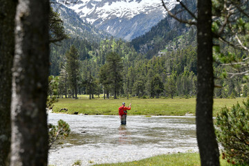 fly fisherman trout fishing with a hiking backpack and an orange jacket in the high mountains in summer