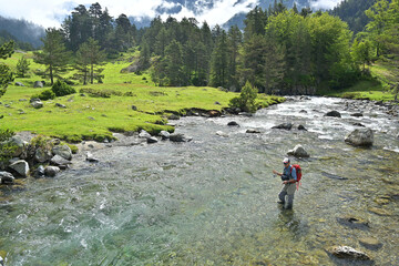 fly fisherman trout fishing with a hiking backpack and a blue shirt in the high mountains in summer