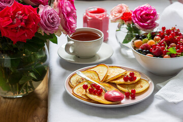 Curd pancakes with berry curd served with tea on a table decorated with bouquets of roses.