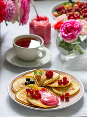 Curd pancakes with berry curd served with tea on a table decorated with bouquets of roses.