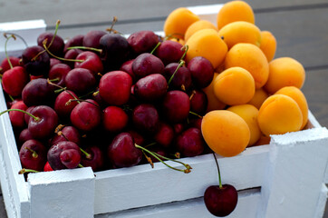 Fresh apricots and cherries in a white wooden box. Half apricots, half cherries. Vegetarian food, supplies. Sale in private gardens. Vitamins Close-up. Copy space.