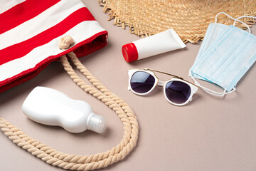 Beach bag with beach items and protective mask on beige background. Coronavirus summer concept