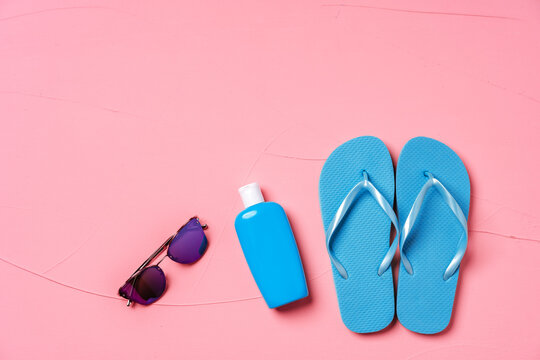Blue flip-flops with sunscreen and sunglasses on pink background