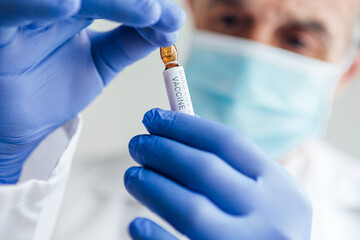 Doctor's hand with blue glove holding container with COVID-19 vaccine