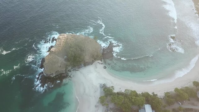 A top-down drone shot of an idyllic Koka Beach. Hidden gem of Flores, Indonesia. Headland going straight into the open sea. Beauty in the nature. Calm waves washing the cliff's slopes. Serenity. 
