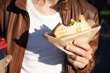 Fast food sandwich fried in the hands of a guy, bitten off. Snack toast on the street