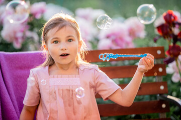 girl blows soap bubbles on the background of flowers in the garden. On the face of emotions of...