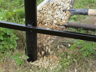 Reinforcement the pillars of the base of the new metal fence with pebble, rubble falls from the shovel
