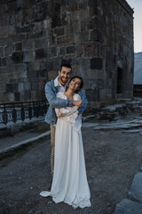 Young Georgian couple posing in the mountains. Boho wedding in Georgia. Evening setting sun. Blue jeans jacket