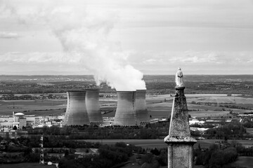 statue of holy watching smoking cooling towers of a nuclear power plant in the coutryside