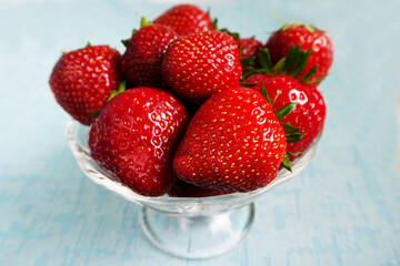 berries of red ripe strawberries in a glass transparent plate on a blue background side view