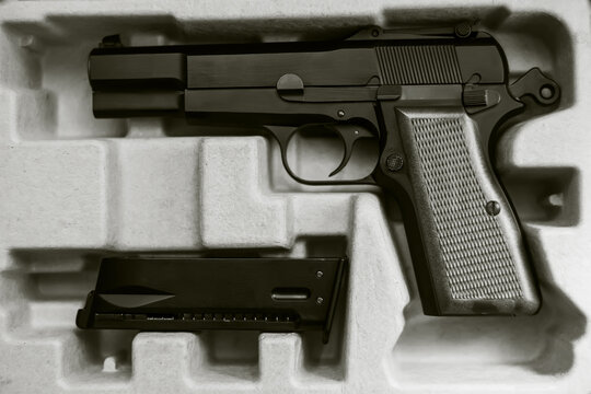 Black-and-white image of the purchased gun and its magazine in a cardboard box. Purchase of weapons. Danger.