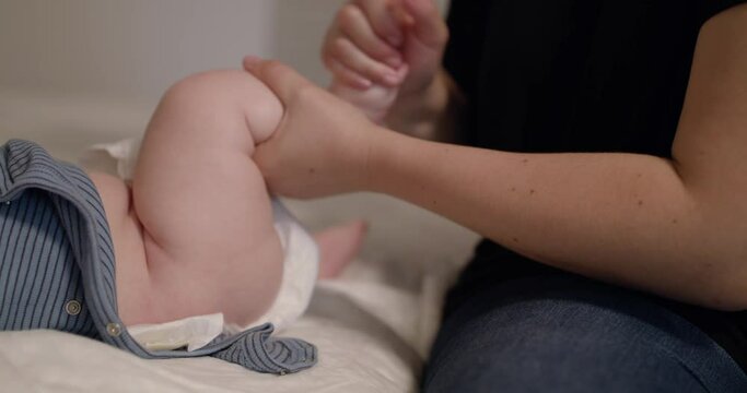 Female hands massages baby's foot on bed in home