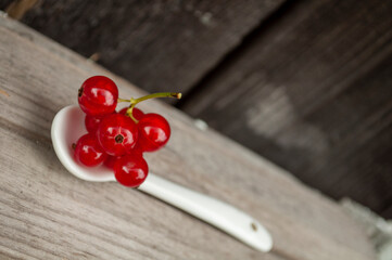 a sprig of red currants lies on a white spoon on a wooden background. minimalism concept, harvest, place for text