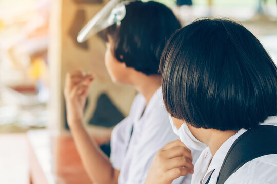 Female Elementary School Student Wear Face Mask To Prevent The Coronavirus(Covid-19) Wait For Her Parents To Pick Her Up To Return Home After School And The Rain Just Stop In Front Of The School Gate