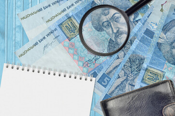 5 Ukrainian hryvnias bills and magnifying glass with black purse and notepad. Concept of counterfeit money. Search for differences in details on money bills to detect fake