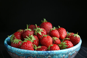 Delicious ripe strawberries in bowl on black background, closeup