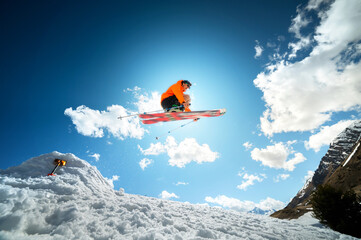 A young stylish man in sunglasses and a cap performs a trick in jumping with a kicker of snow...