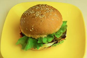 On a yellow ceramic plate lies a large sandwich. Plate shot close-up on a beige wooden table