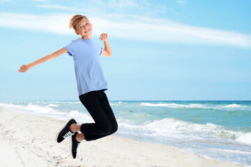 Obraz premium Happy school boy jumping on beach near sea. Summer holidays