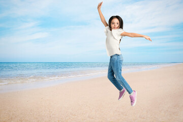Fototapeta premium Cute school girl jumping on beach near sea, space for text. Summer holidays