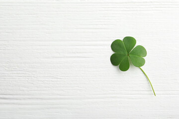 Clover leaf on white wooden table, top view with space for text. St. Patrick's Day symbol