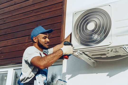 Repairman In Uniform Installing The Outside Unit Of Air Conditioner