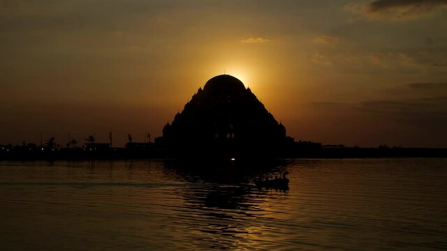 The sun setting behind the 99 domes mosque with a boat passing in the foreground