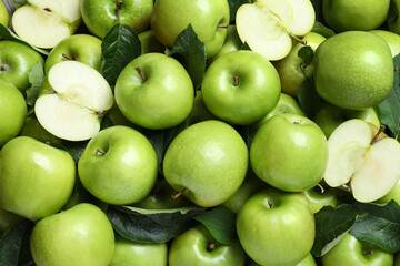 Pile of tasty green apples with leaves as background, top view