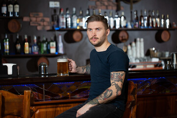 Young man sitting at bar counter with a pint of light beer