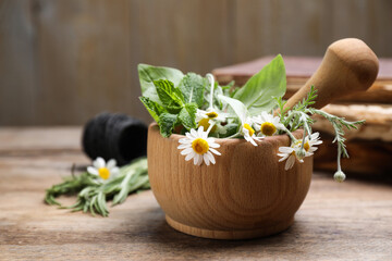 Mortar with chamomile flowers and fresh green mint on wooden table. Healing herbs