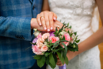 Hands of the bride and groom on a wedding bouquet. Wedding rings