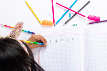 Cute left-handed girl is writing with a pencil in her notebook.