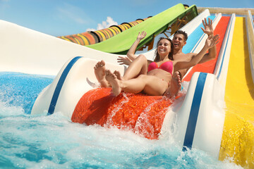 Happy couple on slide at water park, low angle view. Summer vacation