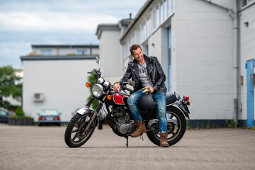 Fototapeta na wymiar Ein Mann sitzt seitlich auf seinem Motorrad und lächelt freundlich 