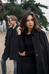 Young couple in the forest. Love story, black coat and dried flowers.