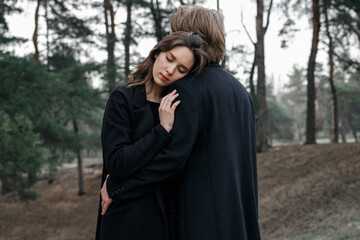 Young couple in the forest. Love story, black coat and dried flowers.