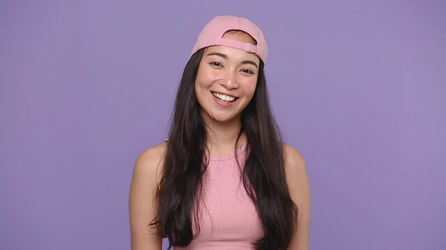 Young cute asian woman girl 20s years old in casual pink clothes cap posing isolated on pastel purple violet background studio. People sincere emotions lifestyle concept. Looking camera charming smile