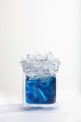 Blue matcha tea with ice in a glass glass on a light background. Vertical photo. Copy of the space.