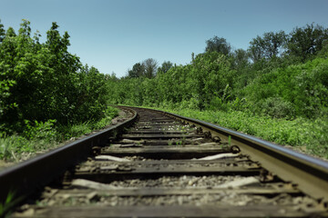 Natural landscape background. Close-up of railroad through green forest in sunny day. Travel concept.
