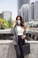 Young female entrepreneur talking on the phone outside a business area.  She wears formal clothes and a medical mask. Selective focus. Business and new normal concept. 