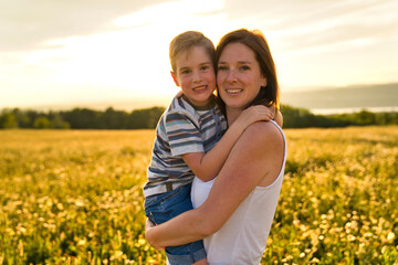 happy family of mother and child on field at the sunset having fun