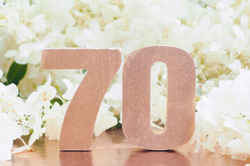 voluminous rose-gold number "70" and many white hydrangea flowers.