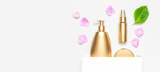 Cosmetic mock up gold bottles. Cosmetics, white gift bag, pink hydrangea flowers on light...
